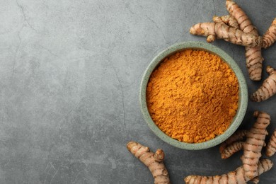 Photo of Bowl with turmeric powder and raw roots on grey table, flat lay. Space for text