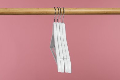 Photo of White clothes hangers on wooden rack against pink background