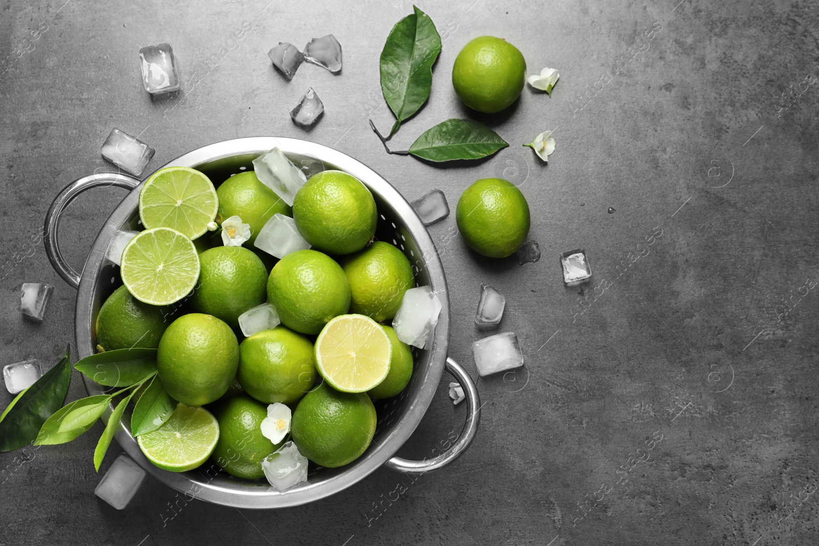 Photo of Colander with fresh ripe limes and ice cubes on gray background, top view