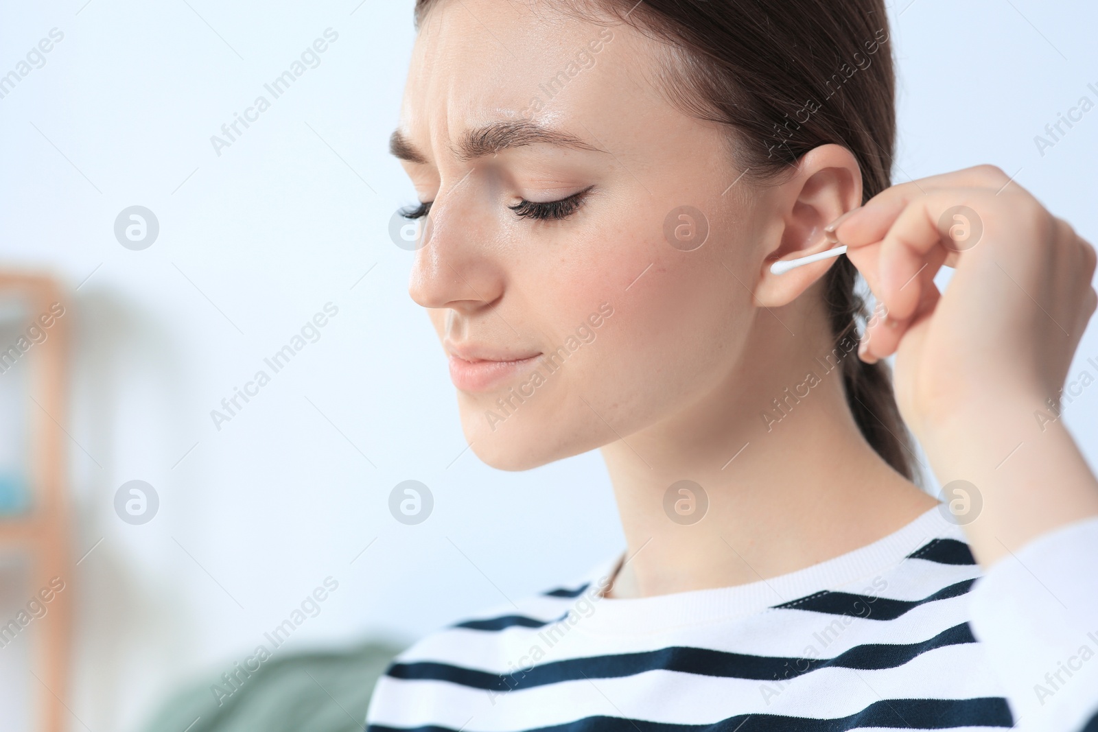 Photo of Young woman cleaning ear with cotton swab indoors, closeup