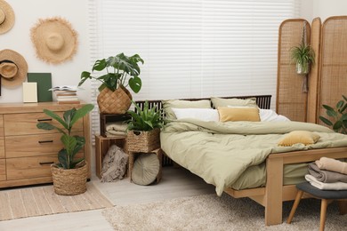 Comfortable bed and beautiful green houseplants in bedroom