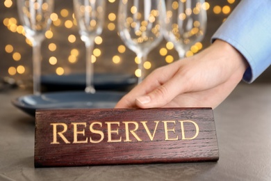 Waiter setting RESERVED sign on restaurant table, closeup