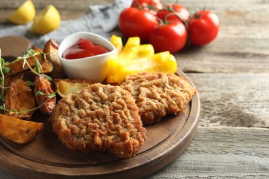 Photo of Tasty schnitzels served with potatoes, ketchup and vegetables on wooden table, closeup