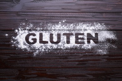 Photo of Word Gluten written with flour on dark wooden table, top view