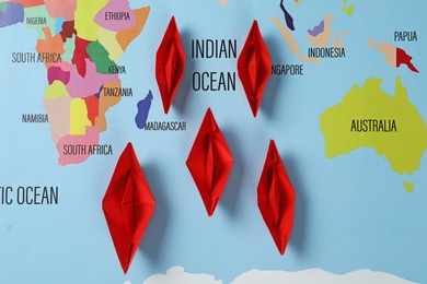 Photo of Red paper boats on world map, flat lay
