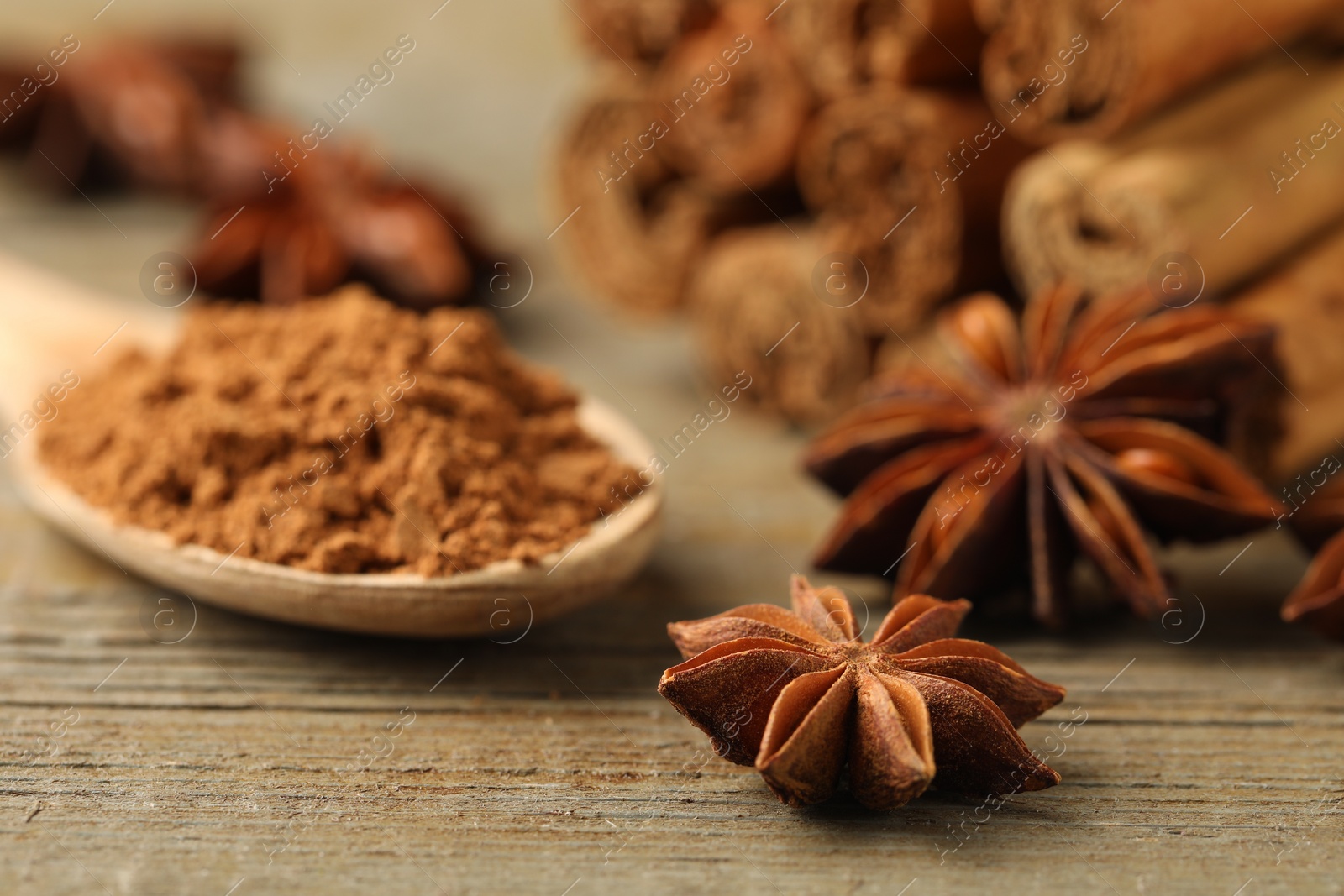 Photo of Spoon with cinnamon powder, sticks and star anise on wooden table, closeup