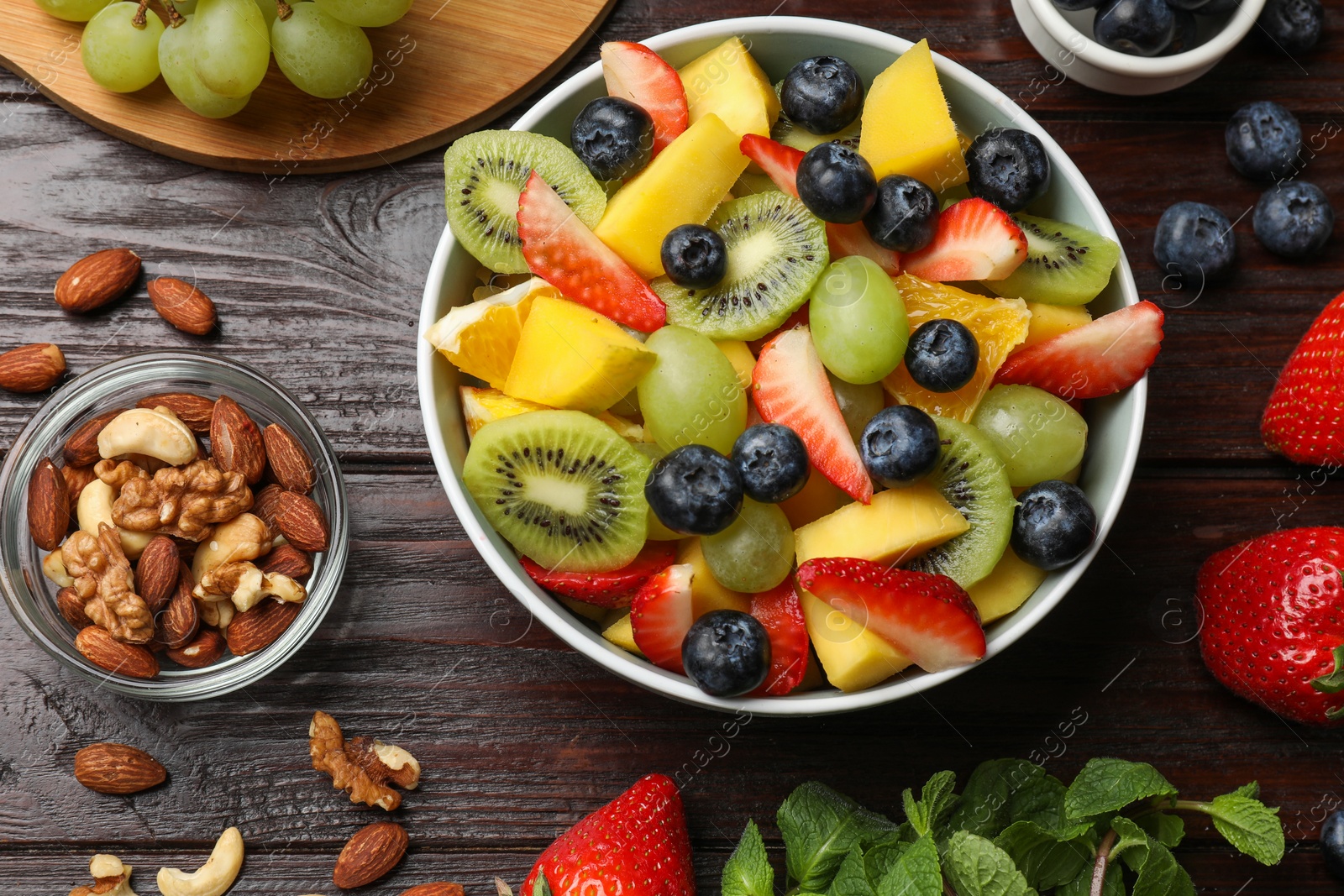 Photo of Tasty fruit salad in bowl and ingredients on wooden table, flat lay