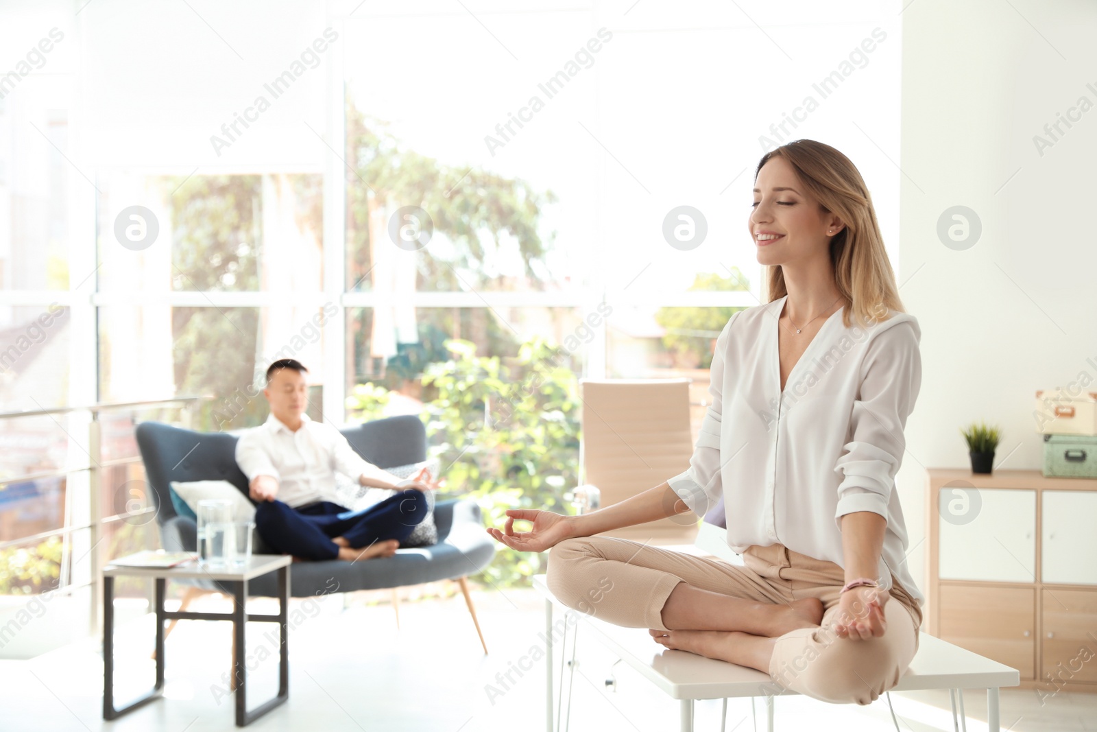 Photo of Young businesswoman and her colleague doing yoga in office. Workplace fitness