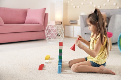 Photo of Cute little child playing with building blocks on floor, indoors