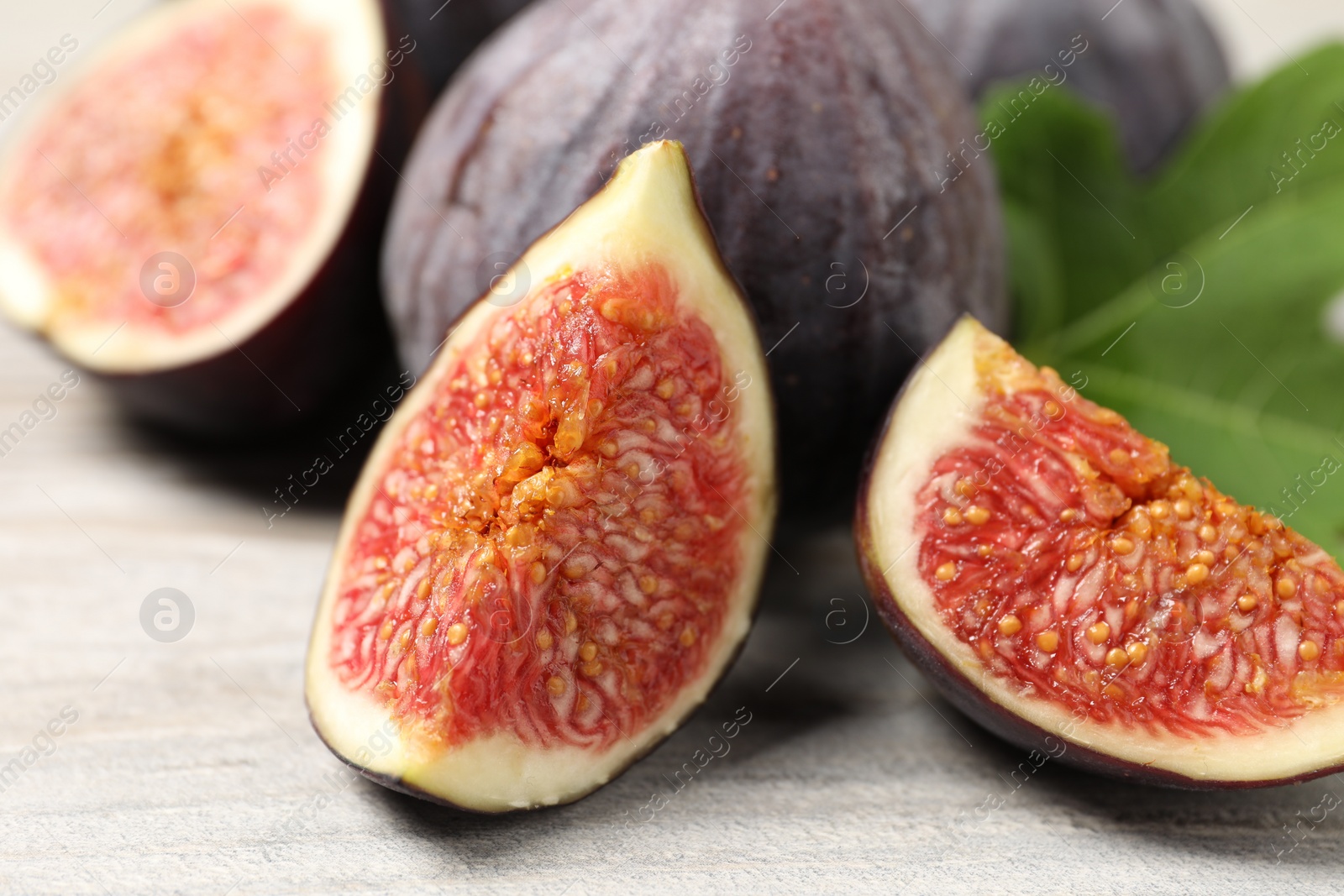 Photo of Whole and cut ripe figs on light wooden textured table, closeup
