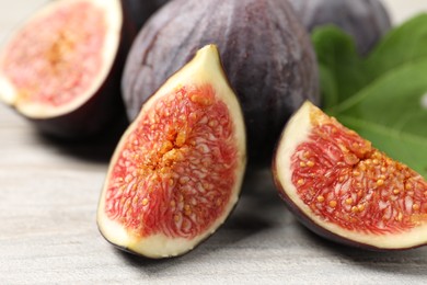 Whole and cut ripe figs on light wooden textured table, closeup