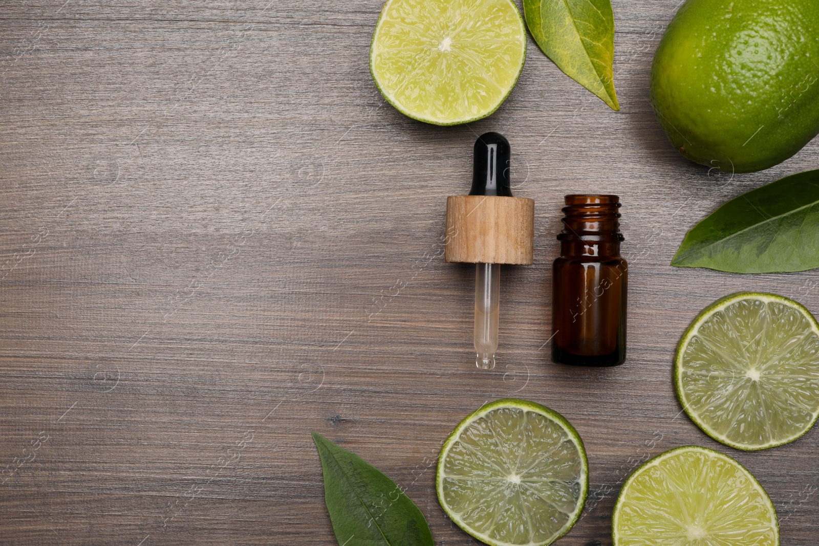 Photo of Bottle of essential oil with lime slices and leaves on wooden table, flat lay. Space for text