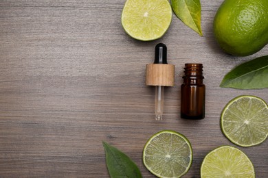 Bottle of essential oil with lime slices and leaves on wooden table, flat lay. Space for text