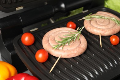 Photo of Electric grill with homemade sausages, rosemary and tomatoes on table, closeup