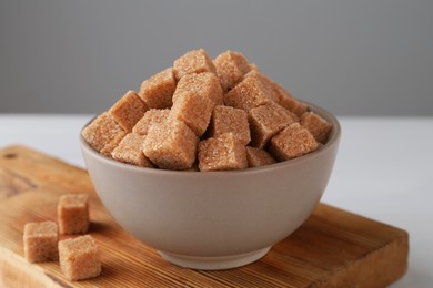 Photo of Brown sugar cubes in bowl on white table, closeup