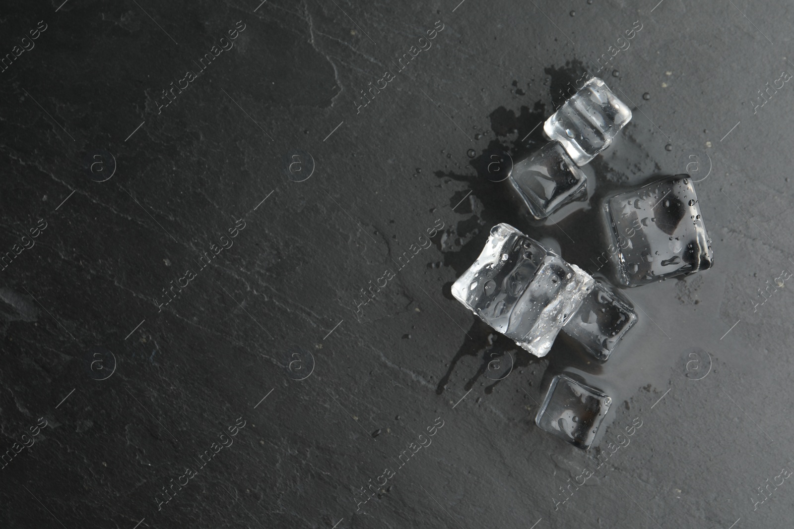 Photo of Crystal clear ice cubes with water drops on black table, flat lay. Space for text