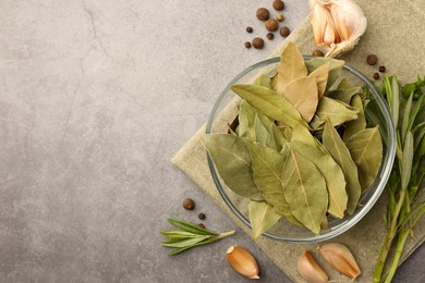 Photo of Aromatic bay leaves in glass bowl, different herbs and spices on light gray table, flat lay. Space for text