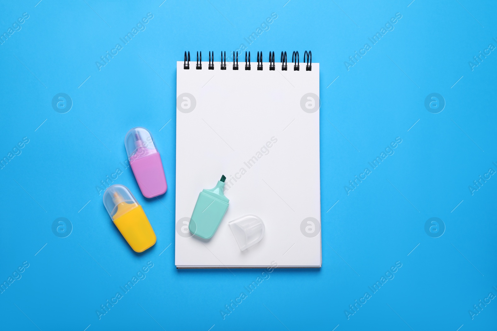 Photo of Open notebook and colorful markers on light blue background, flat lay