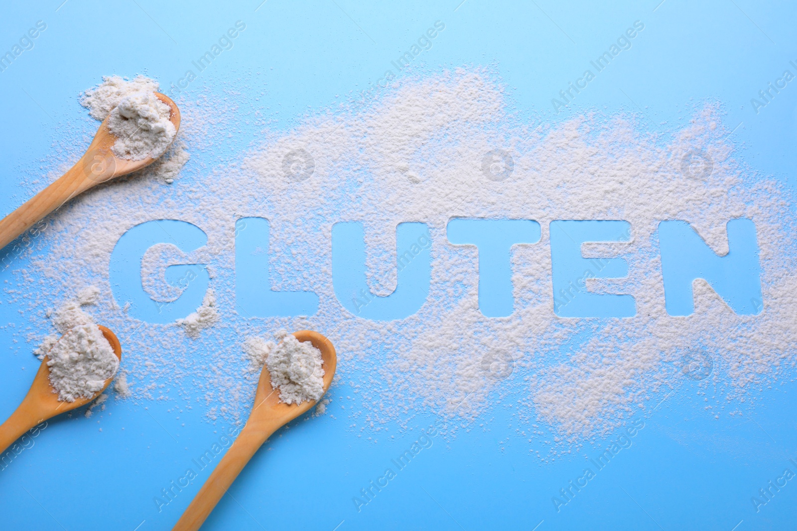 Photo of Spoons and word Gluten written with flour on light blue background, flat lay