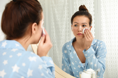 Photo of Teen girl with acne problem cleaning her face near mirror in bathroom