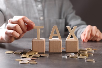 Photo of Woman with word Tax, wooden cubes and coins at grey table, closeup