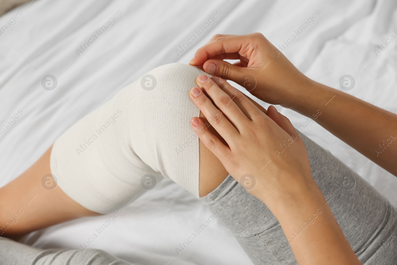 Photo of Young woman with leg wrapped in medical bandage on bed, closeup