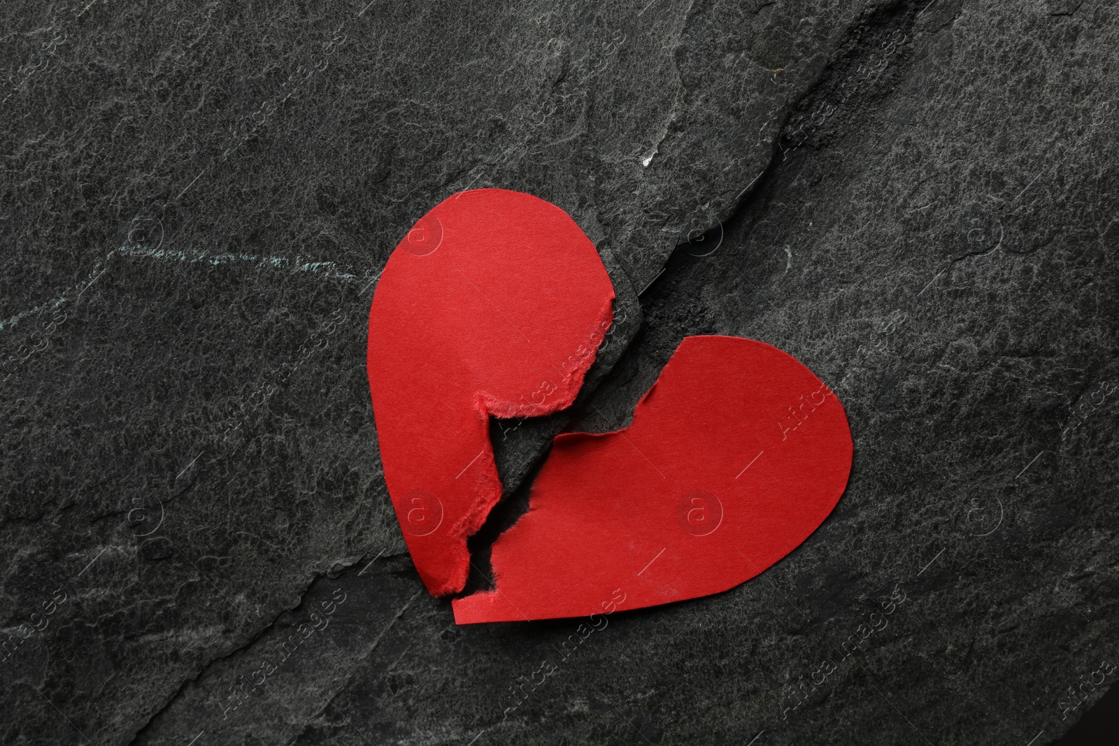 Photo of Halves of torn red paper heart on dark grey table, top view. Broken heart