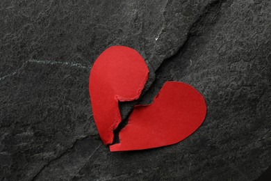 Photo of Halves of torn red paper heart on dark grey table, top view. Broken heart