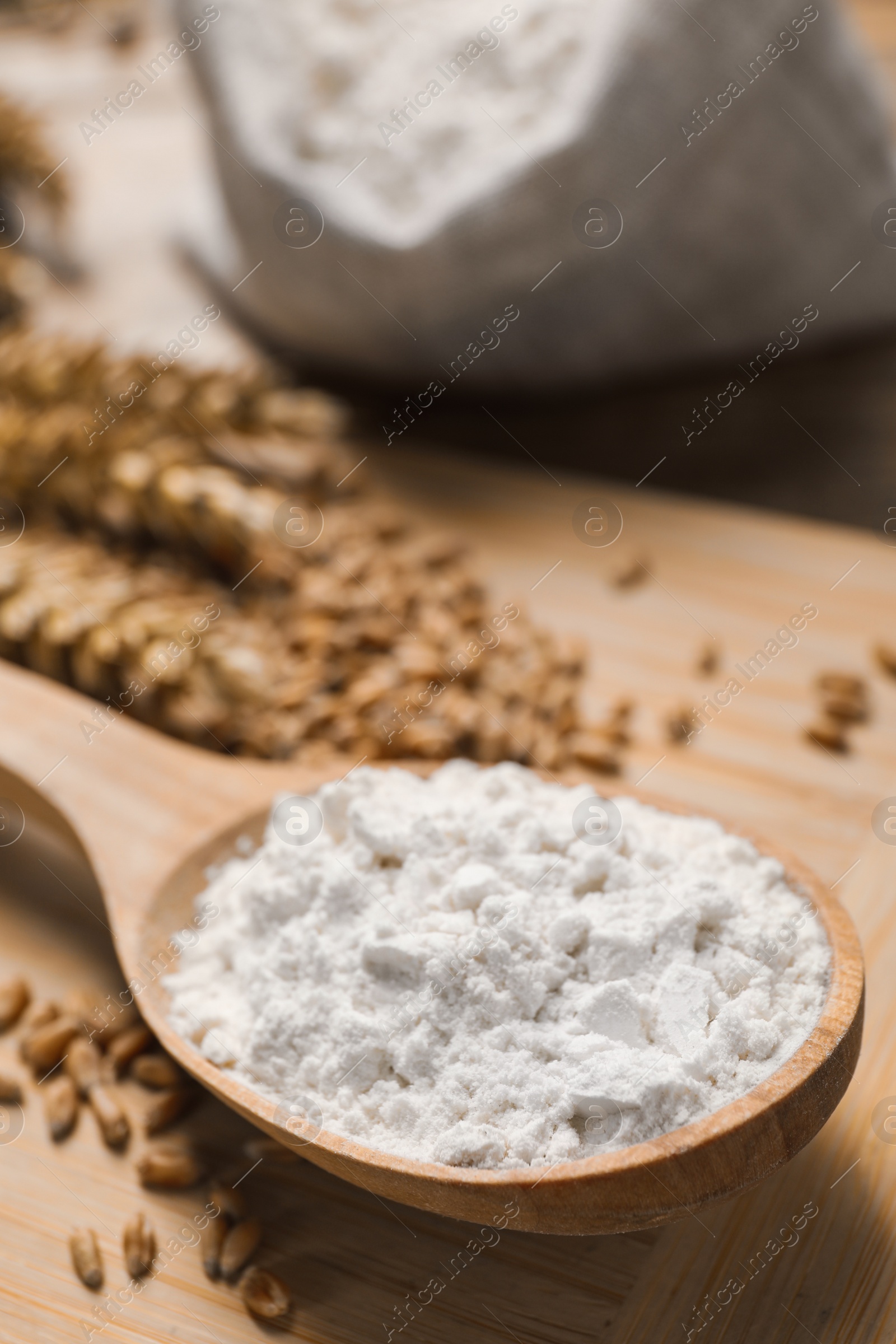 Photo of Spoon with wheat flour and grains on wooden board, closeup