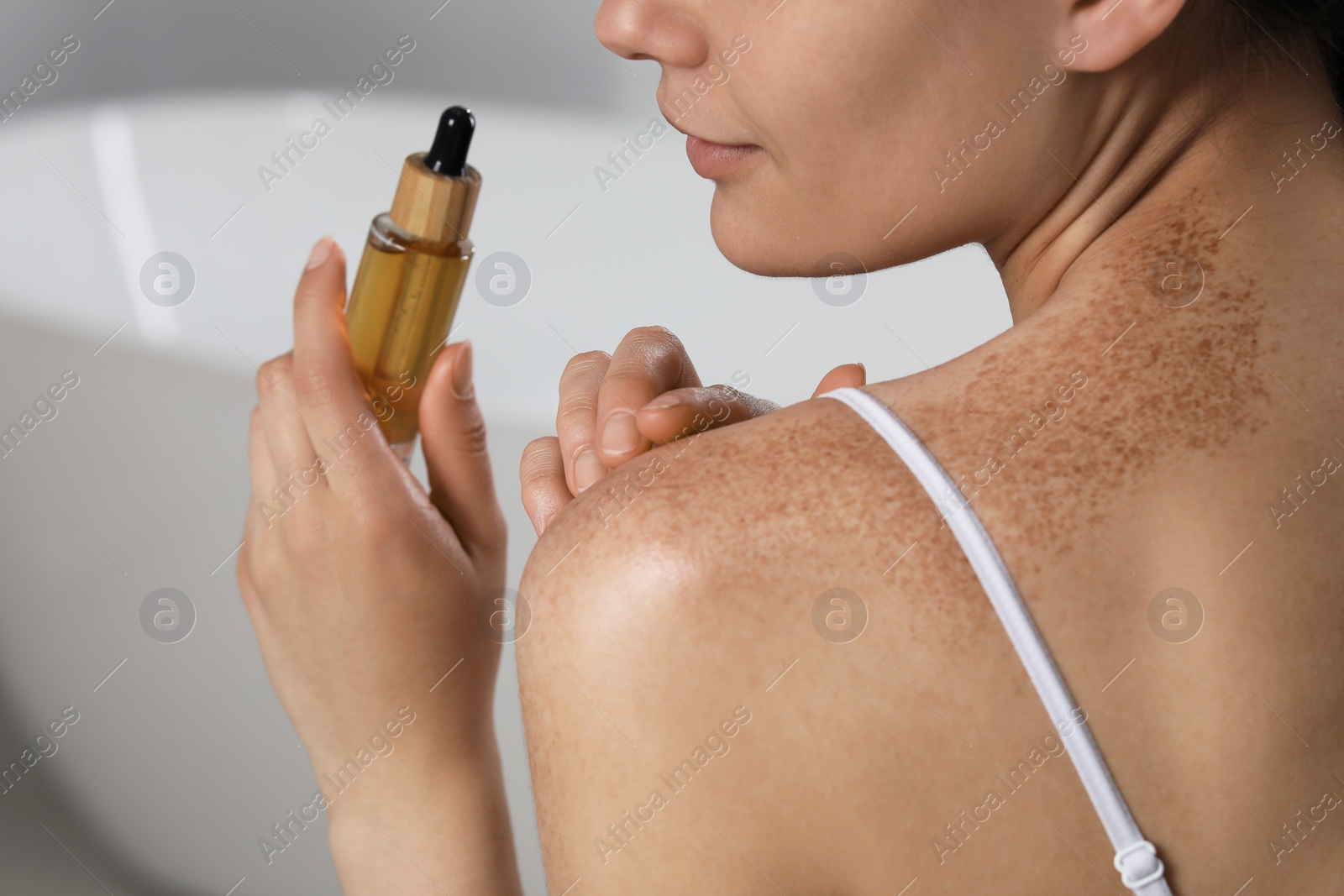 Photo of Young woman holding bottle of body oil in bathroom, closeup