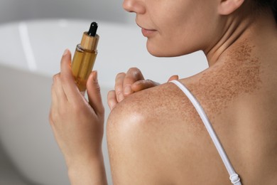 Young woman holding bottle of body oil in bathroom, closeup