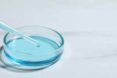 Photo of Dripping liquid from pipette into petri dish at white table, closeup. Space for text