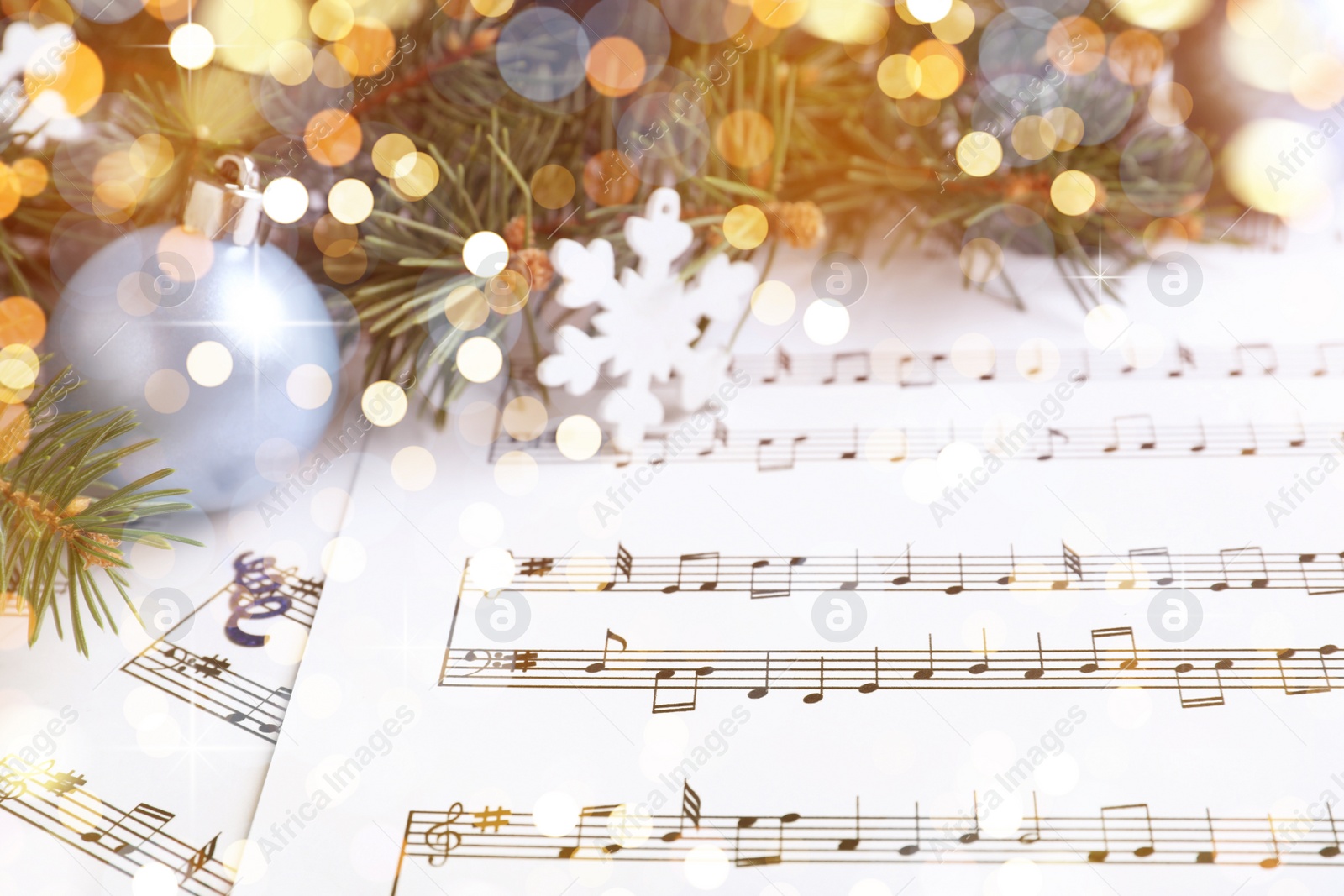 Image of Fir branches, decorative snowflake and light blue balls on Christmas music sheets, closeup. Bokeh effect