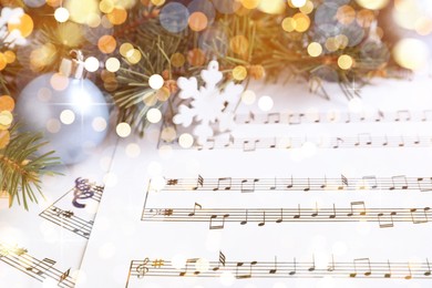 Fir branches, decorative snowflake and light blue balls on Christmas music sheets, closeup. Bokeh effect