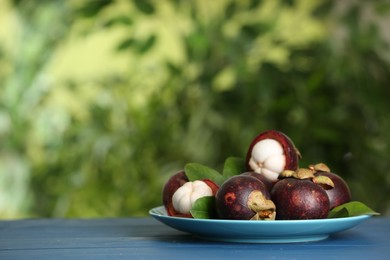 Photo of Delicious ripe mangosteen fruits on blue wooden table outdoors, space for text