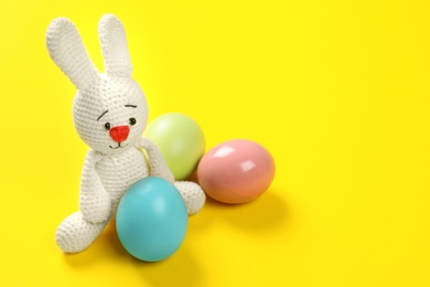 Photo of Cute Easter bunny toy and dyed eggs on color background, space for text