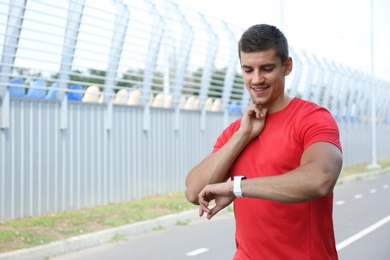 Photo of Young man checking pulse after training outdoors