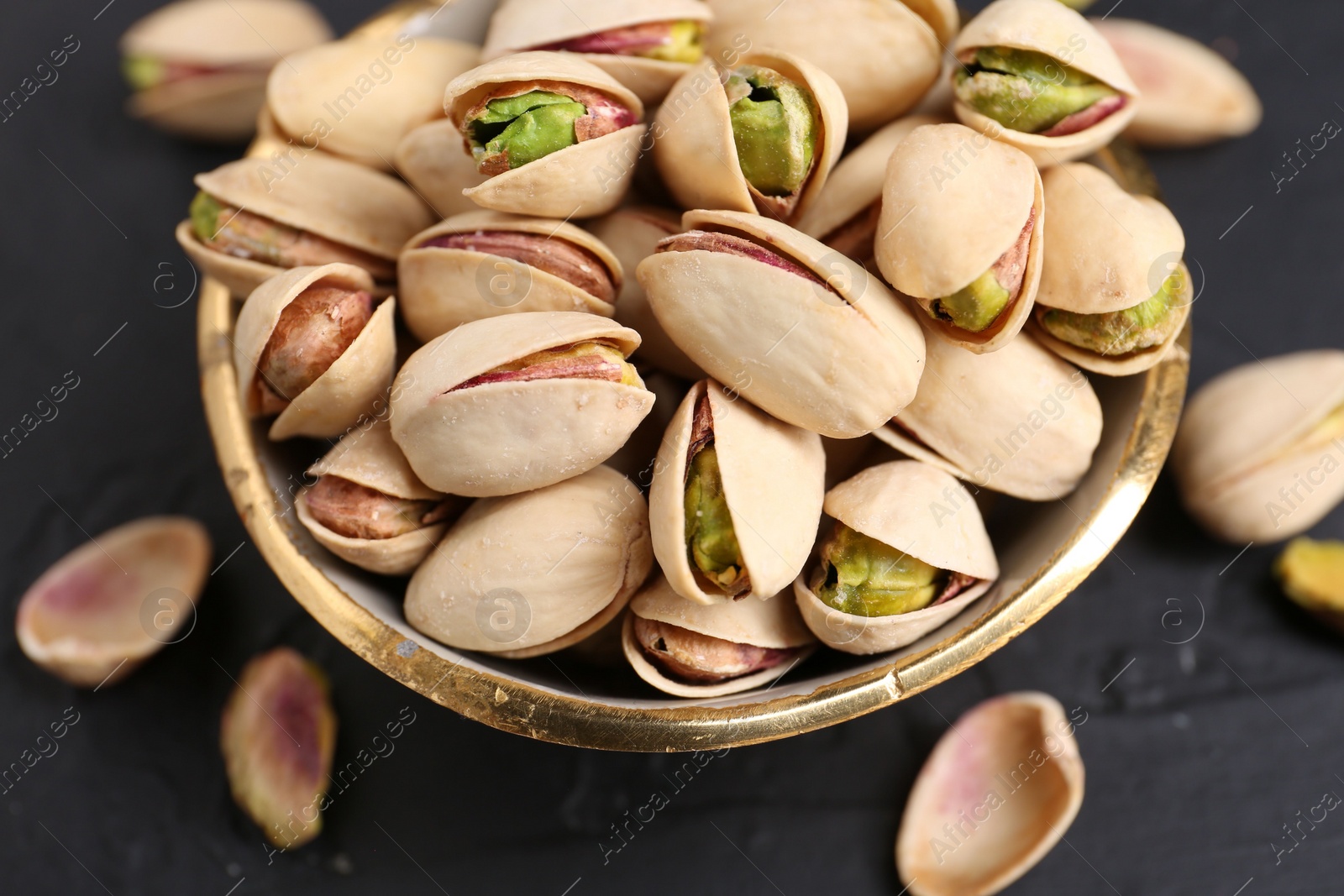 Photo of Tasty pistachios in bowl on black table, closeup