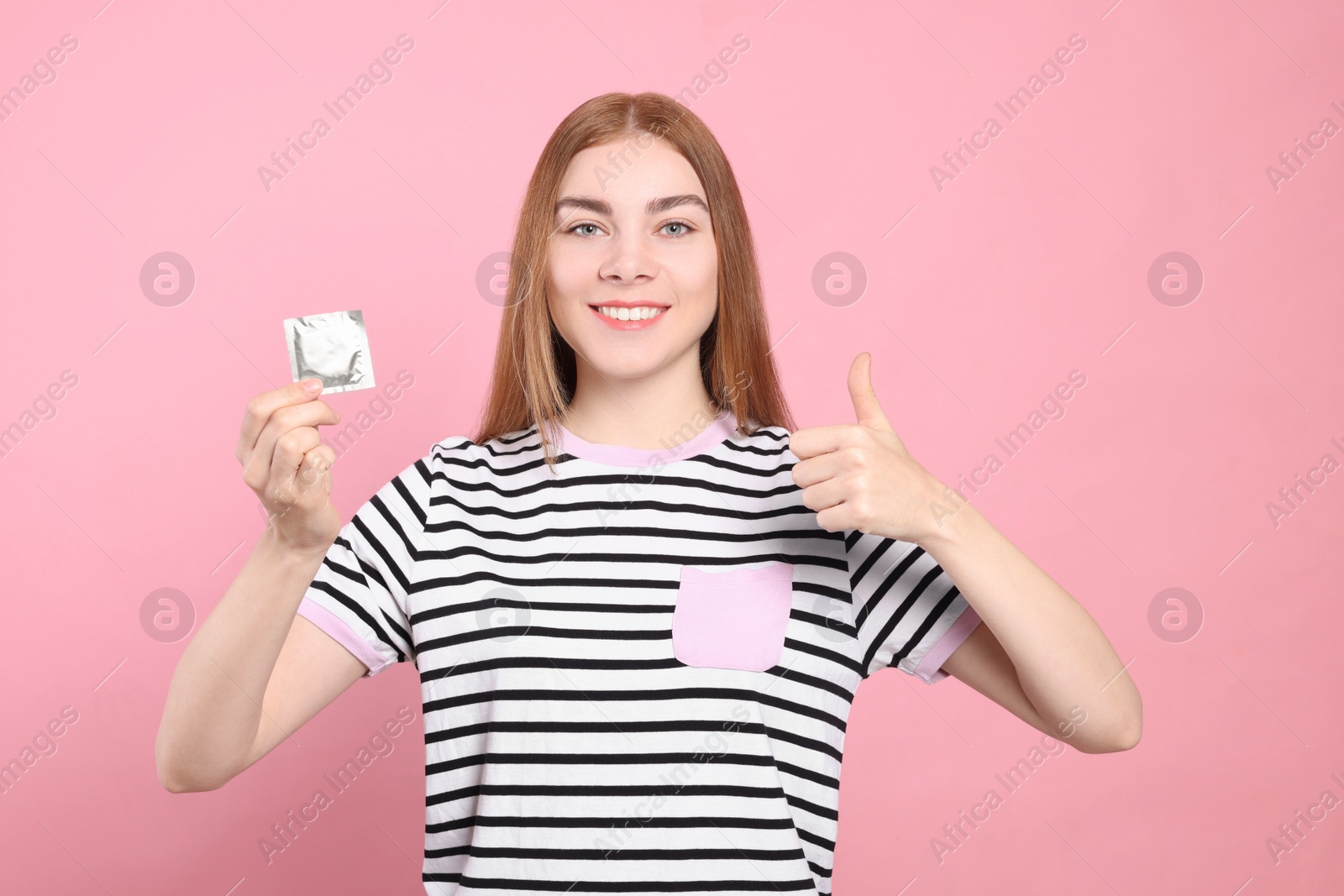 Photo of Woman with condom showing thumb up on pink background. Safe sex