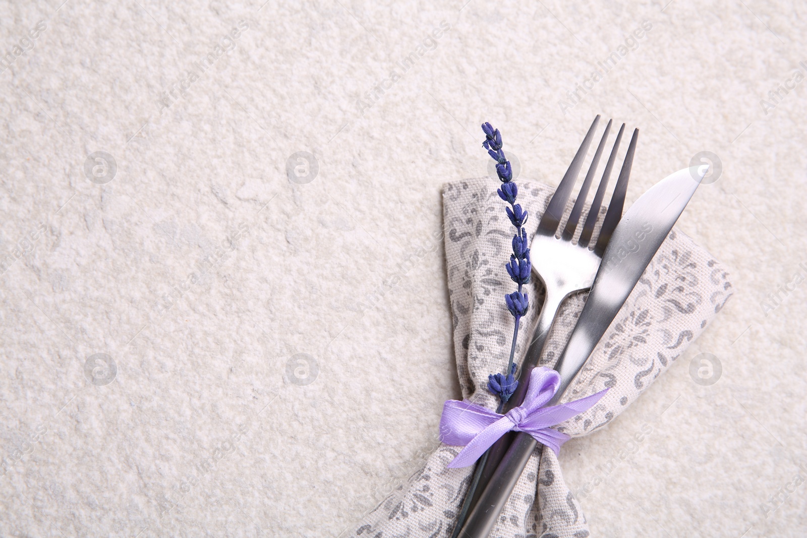Photo of Cutlery, napkin and preserved lavender flower on white textured table, top view. Space for text
