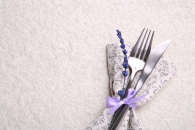 Cutlery, napkin and preserved lavender flower on white textured table, top view. Space for text