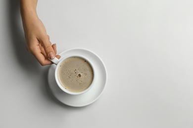 Photo of Woman holding cup of coffee at white table, top view. Space for text