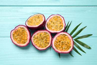 Halves of passion fruits (maracuyas) and palm leaf on light blue wooden table, flat lay