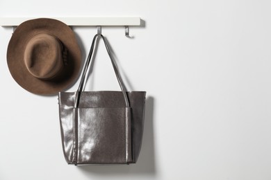 Photo of Brown hat and bag hanging on hook rack on white wall, space for text