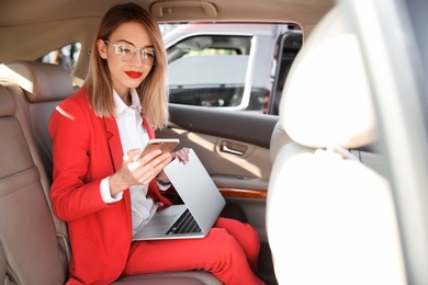 Young businesswoman with smartphone and laptop in car