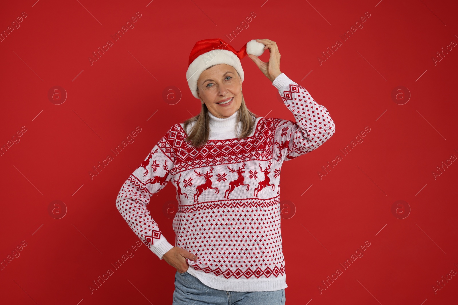 Photo of Happy senior woman in Christmas sweater and Santa hat on red background