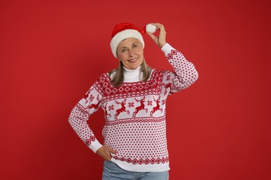 Happy senior woman in Christmas sweater and Santa hat on red background