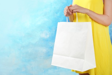 Woman holding paper shopping bag on color background