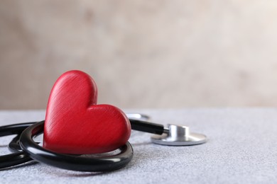 Photo of Stethoscope and red heart on grey stone table. Space for text