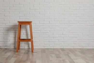 Photo of Stylish wooden stool near white brick wall indoors. Space for text